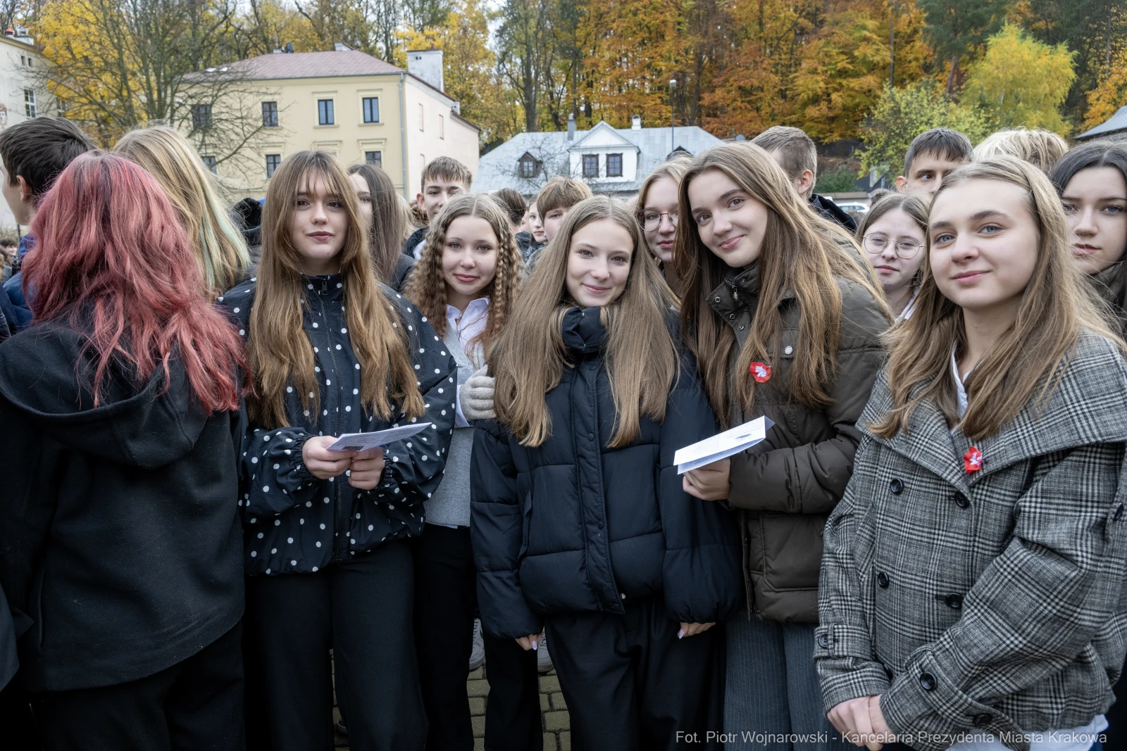 Grupa uczniów w różnych strojach, uśmiechniętych, z kartkami w rękach, w tle kolorowe drzewa.  Autor: Piotr Wojnarowski