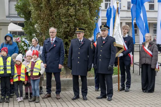 Uczestnicy uroczystości patriotycznej z flagami i odznaczeniami.