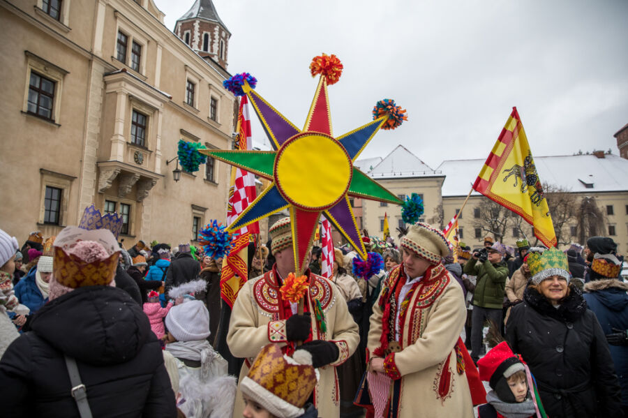 Orszak Trzech Króli 2021. Wyruszający ze wzgórza Wawelskiego. Na czele pochodu mężczyzna w stroju krakowskim niosący dużą żółtą gwiazdę betlejemską, której ramiona są ozdobione kolorowymi pomponami. 