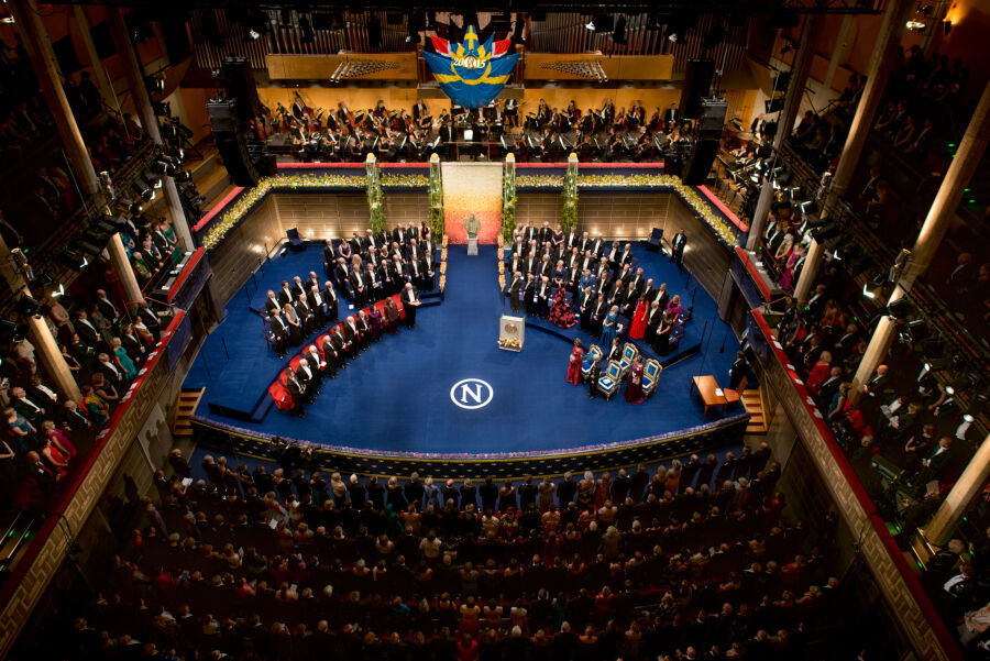 Ceremonia noblowska w 2015 roku. Widok ogólny z góry na wypełnioną elegancko ubranymi gośćmi wydarzenia miejsce uroczystości którym jest sala koncertowa. 
