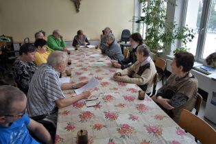 Spotkanie ze sceną 22.12.2022 r. na zdjęciu widać grupę osób przy długim stole. trzymają w dłoniach kartki z tekstami. Przygotowują się do przedstawienia teatralnego.