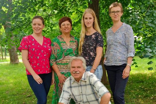 Na zdjęciu widzimy grupę czterech kobiet i jednego mężczyzny stojących na tle zielonych drzew. 