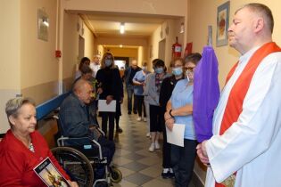 Droga Krzyżowa 02.04.2021 kilkanaście osób uczestniczących w Drodze Krzyżowej.
Na pierwszym planie ksiądz trzymający w rękach krzyż, obok starsza kobieta na wózku inwalidzkim trzymająca obraz stacji drogi krzyżowej