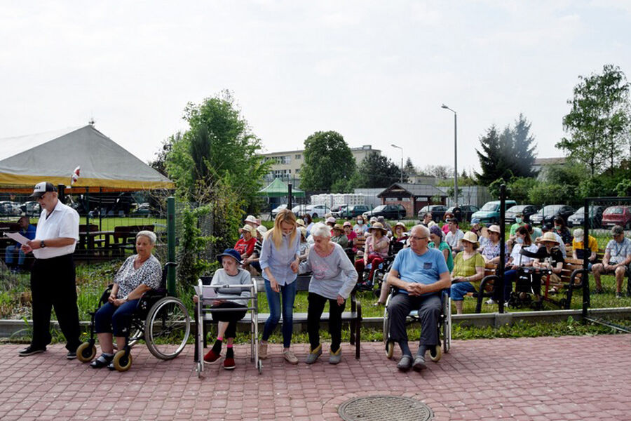 Zdjęcie przedstawia uczestników nabożeństwa, które odbywa się w plenerze. Na pierwszym planie znajduje się sześć osób. Za nimi na ławkach siedzi jeszcze około trzydzieści osób.