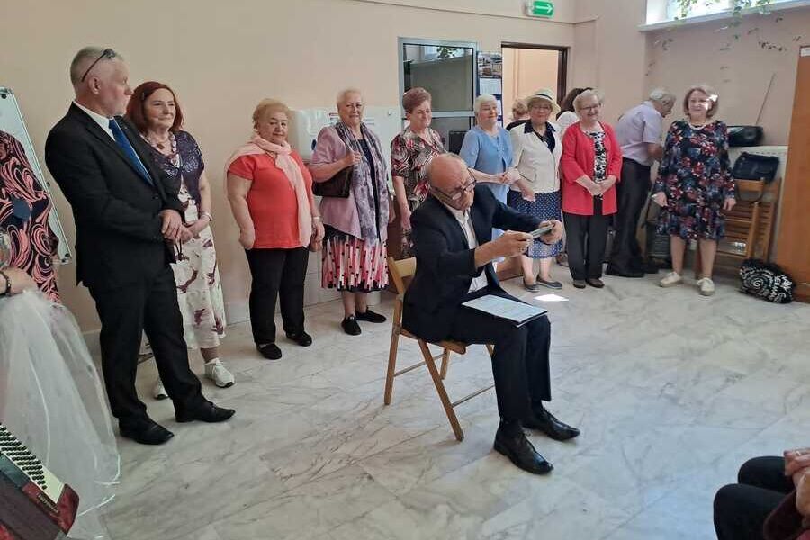 Aktor siedzi na krześle i „walczy” z pilotem od telewizora