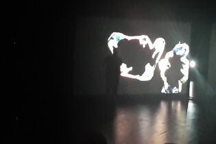 Widoczny w ciemności ekran z projekcją treści performatywnej