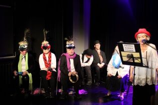 XXI Przegląd Teatralno-Muzyczny O BUŁAWĘ LAJKONIKA 30.03.2023 Grupa kobiet i mężczyzn w kostiumach teatralnych. Na pierwszym planie kobieta stojąca przy mikrofonie za pulpitem nutowym.