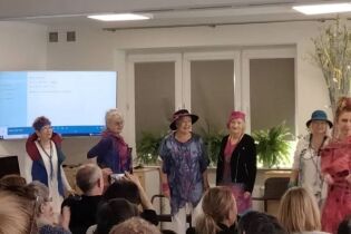 Grupa kobiet w pomieszczeniu prezentujących stroje. 

