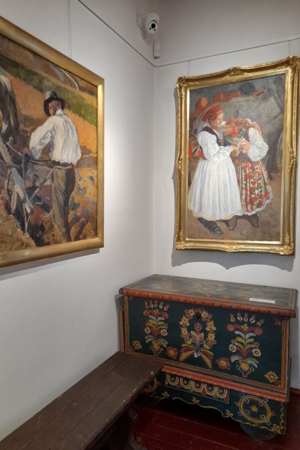 Obrazy na ścianach i zabytkowa, malowana skrzynia w pomieszczeniu.