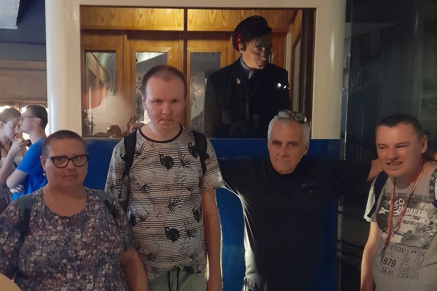 Kobieta i 3 mężczyźni stojący w pomieszczeniu na tle makiety tramwaju z manekinem w stroju konduktora.