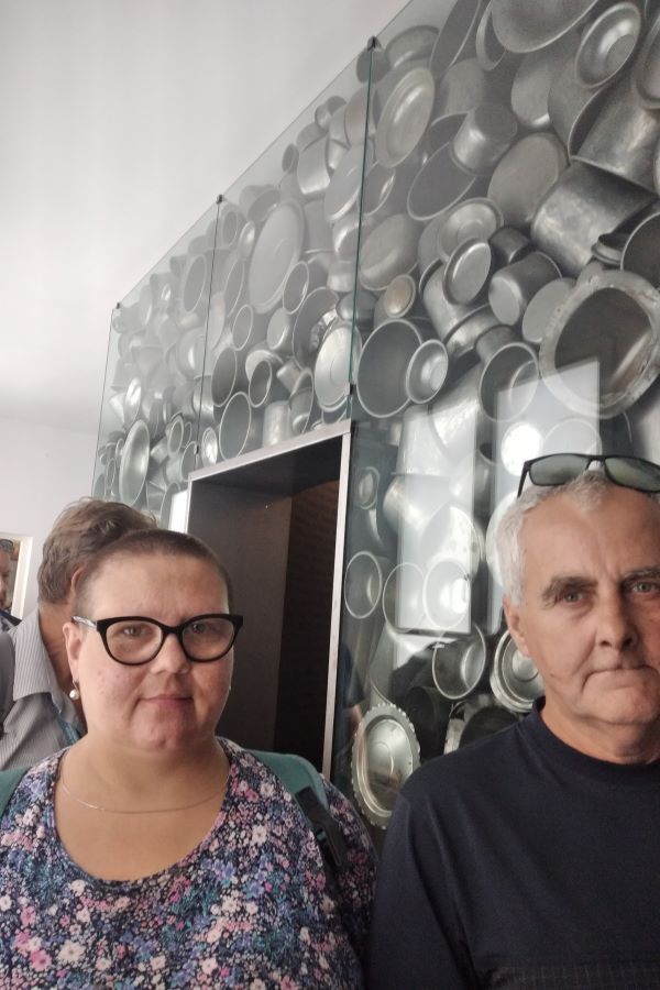 Kobieta i mężczyzna na tle szklanej ściany, która wypełniona jest blaszanymi naczyniami.