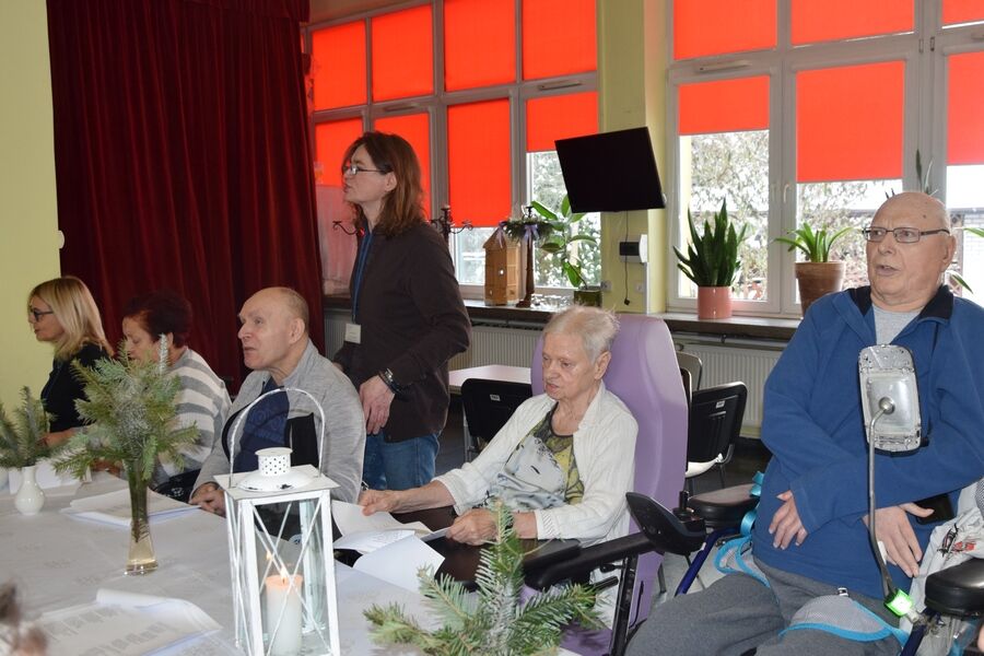 Mieszkańcy, instruktor terapii wraz z dyrektorem podczas śpiewania kolęd