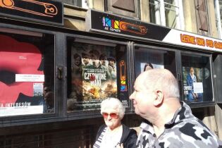 „Czerwone maki” Kobieta i mężczyzna na tle budynku z fotosami w gablotach.