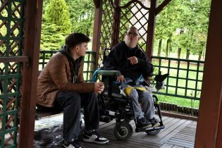 Spotkania ze sceną 19.04.2024 Mieszkaniec na wózku rozmawia z licealistą w altance ogrodowej.