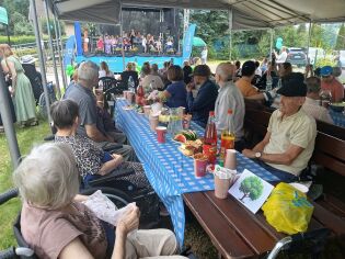 Piknik rodzinny na Łanowej 43 26.06.2024 Uczestnicy pikniku siedzą w ogrodzie przy stołach, oglądają występy na scenie.