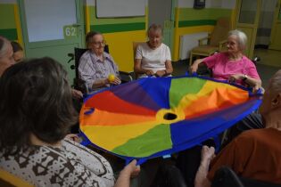 Zajęcia sensoryczne 27.06.2024 Mieszkańcy siedzą w kole, trzymają chustę klanza.