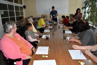 Trening procesów poznawczych 01.07.2024 Kilkunastu mieszkańców siedzi przy długim stole.