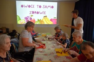 Inspirujące wtorki 02.07.2024 Kilkoro mieszkańców siedzi przy długim stole, kroją owoce.