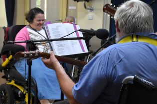 Zajęcia muzyczne 04.07.2024 Mieszkaniec gra na gitarze, przed nim mieszkanka na wózku.