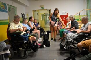 Zajęcia sensoryczne 11.07.2024 Kilkoro mieszkańców siedzi w rzędzie przed nimi pies rasy border-collie.