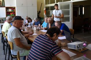 Procesy poznawcze 29.07.2024 Kilkunastu mieszkańców siedzi przy długim stole, rozwiązują zadania.
