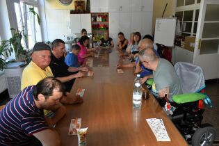 Zawody 31.07.2024 Kilkunastu mieszkańców siedzi przy długim stole, przed sobą maja kartki z liczbami.