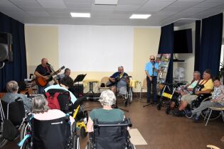 Zajęcia muzyczne 01.08.2024 Kilkunastu mieszkańców słucha występu trzech gitarzystów i klarnecisty.