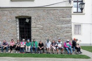 Sucha Beskidzka 28.06.2024 Grupa kobiet i mężczyzn siedzących na murku na tle podmurówki zamku.