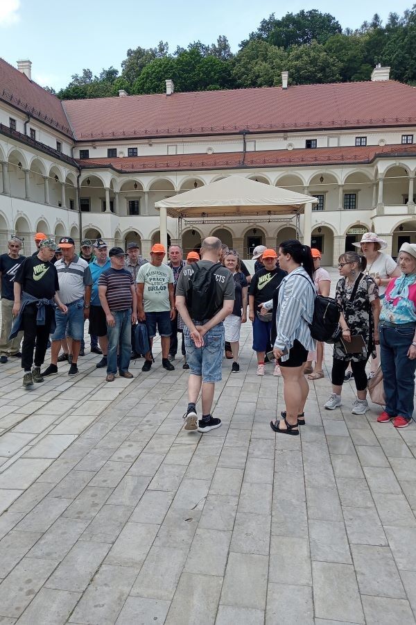 Grupa kobiet i mężczyzn stojących na dziedzińcu zamku ozdobionym arkadowymi krużgankami.