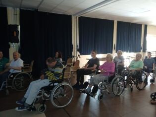 Mieszkańcy siedzą w świetlicy domu, oglądają film.