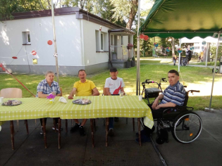 Mistrzostwa Prasko Olimpijskie 07.08.2024 Czterech mieszkańców siedzi przy stole w ogrodzie. Odpoczywają po zmaganiach sportowych.