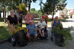 Wycieczka po ziele 14.08.2024 Grupa sześciu mieszkańców z opiekunem pozują do zdjęcia, trzymają na rękach zioła i kwiaty.