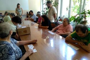 Turniej lotto 29.08.2024 Kilkunastu mieszkańców siedzi przy długim stole, przed sobą mają kartki z liczbami.