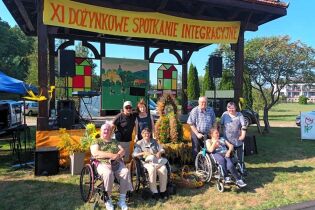 Dożynki 05.09.2024 Siedmioro mieszkańców wraz z opiekunami na tle sceny i wieńców dożynkowych.