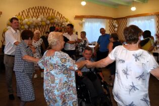 Dzień Działkowca 07.09.2024 Kilkanaście osób tańczy w kółeczku, w środku nasz mieszkaniec na wózku.