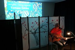 Koncert Tomasza Żółtko 12.09.2024 Wykonawca gra na gitarze na tle ozdobnego parawanu.