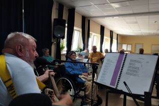 Zajęcia muzyczne 19.09.2024 Mieszkaniec na wózku gra na gitarze przed nim siedzą mieszkańcy.