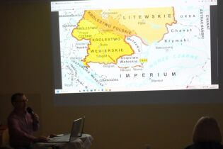 Koło historyczne 11.10.2024 Pan Dyrektor siedzi przy laptopie, w ręce trzyma mikrofon, na ekranie duża mapa XV-wiecznej Europy.