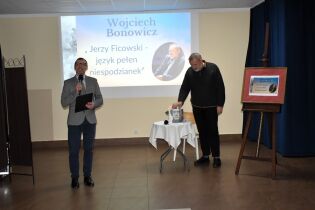 Spotkanie z Wojciechem Bonowiczem 13.11.2024 Pan Dyrektor z mikrofonem obok Pan Wojciech Bonowicz.