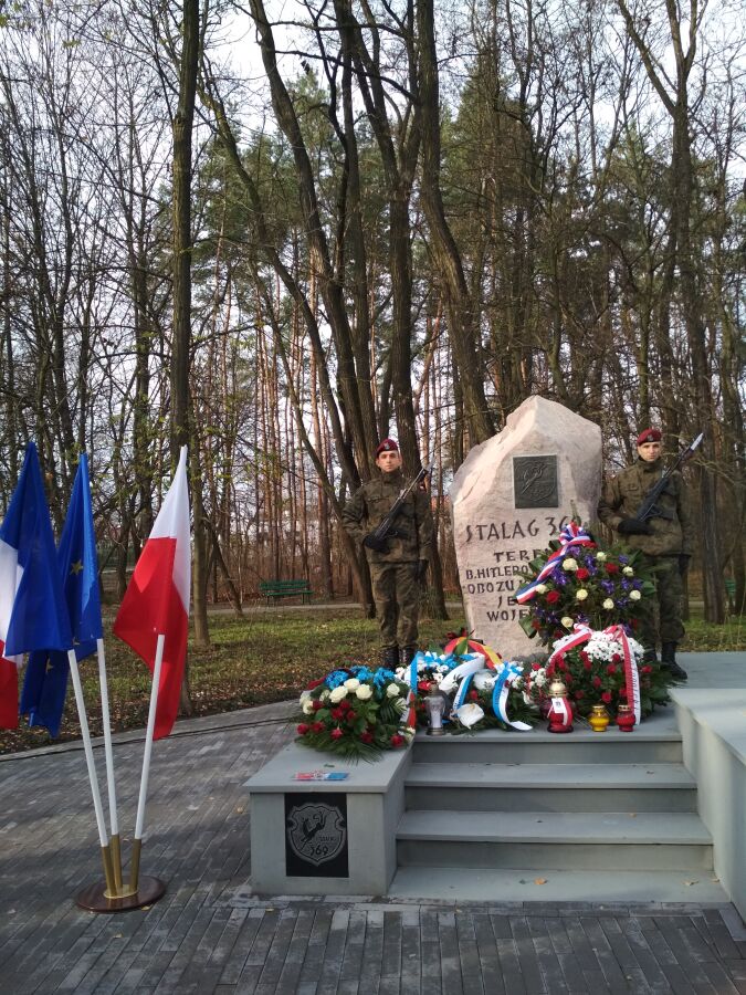 Upamiętnienie więźniów Stalagu 369. Warta 2 żołnierzy przy obelisku oraz wiązanki kwiatów złożone pod pomnikiem.    