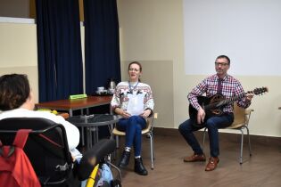 Muzykoterapia 02.12.2024 Pan Dyrektor gra na gitarze, terapeutka śpiewa, przysłuchuje się mieszkanka na wózku.