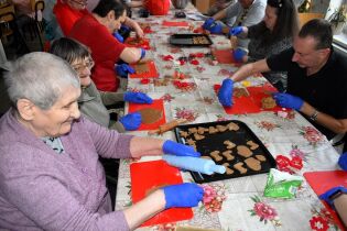 Zajęcia terapeutyczne 06.12.2024 Kilkunastu mieszkańców siedzi przy długim stole, wałkują ciasto.