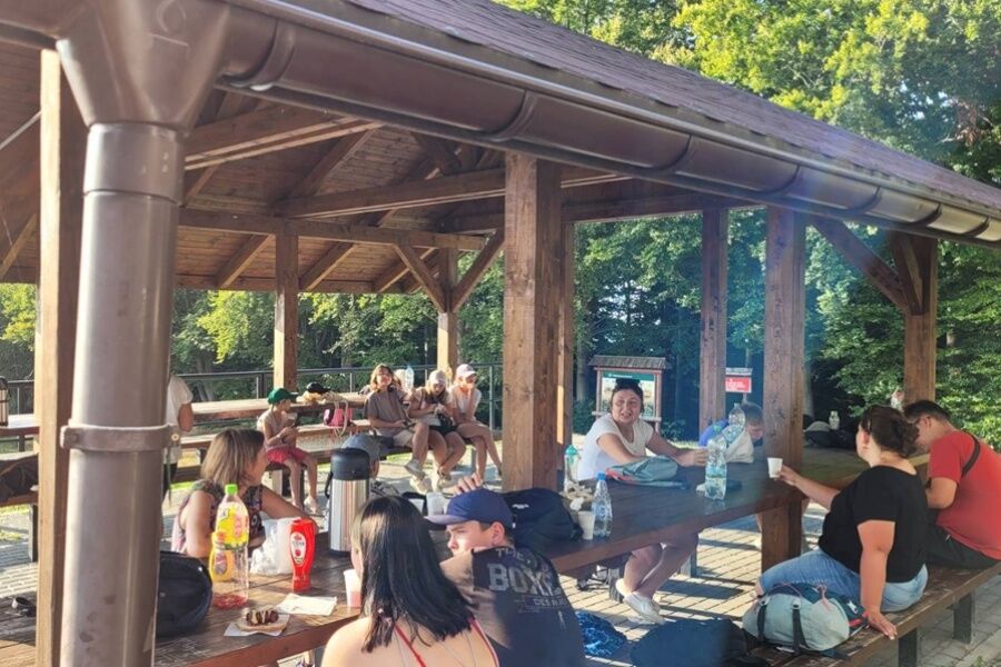 grupa dzieci siedzi pod drewnianą wiatą