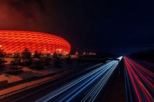 Grafika przedstawia stadion z zewnątrz, podświetlony na czerwono.