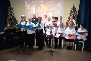 Kilkunastu seniorów w odświętnych strojach śpiewa kolędy.