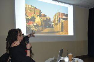 Literackie wędrówki 05.02.2025 Prowadząca wskazuje na duży slajd na ekranie.