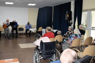 Muzykoterapia 06.02.2025 Kilkunastu mieszkańców słucha zespołu złożonego z dwóch terapeutów i mieszkańca .