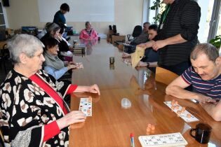 Lotto 20.02.2025 Kilkunastu mieszkańców siedzi przy długim stole, przed sobą mają kartki z numerkami .