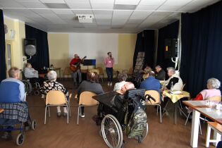 Muzykoterapia 06.03.2025 Kilkunastu mieszkańców słucha dwójki terapeutów.
