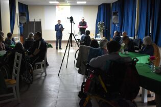 Spotkanie z poezją 13.03.2025 Mieszkańcy siedzą przy stolikach, na przodzie stoją Pan Dyrektor i Redaktor Wojciech Bonowicz.